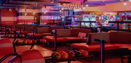 Bowling alley lanes and seating area with an arcade visible in the back