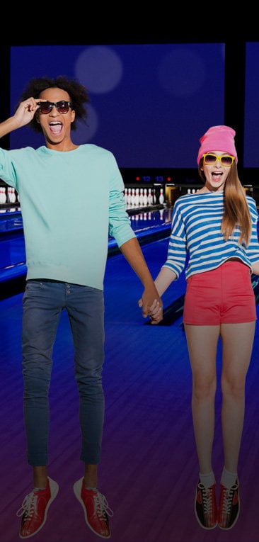 Two teens holding hands and jumping in front of bowling lanes