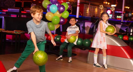 boy bowling with another boy and a girl cheering him on