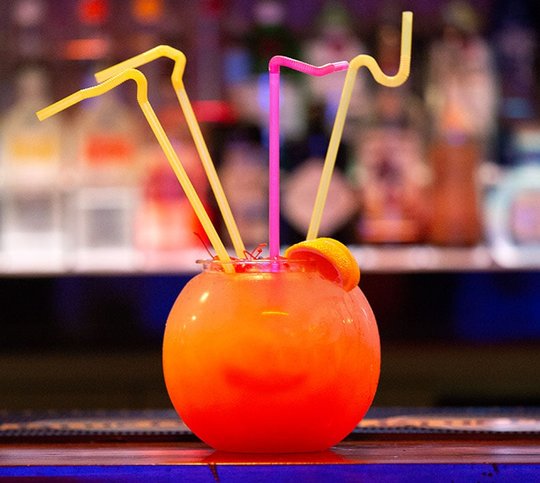 Bright orange drink in a fishbowl with crazy straws in it